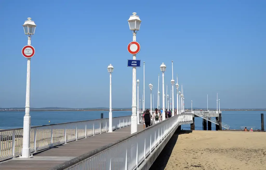 The pier in Arcachon. A wide paved pier leads out and over the beach.