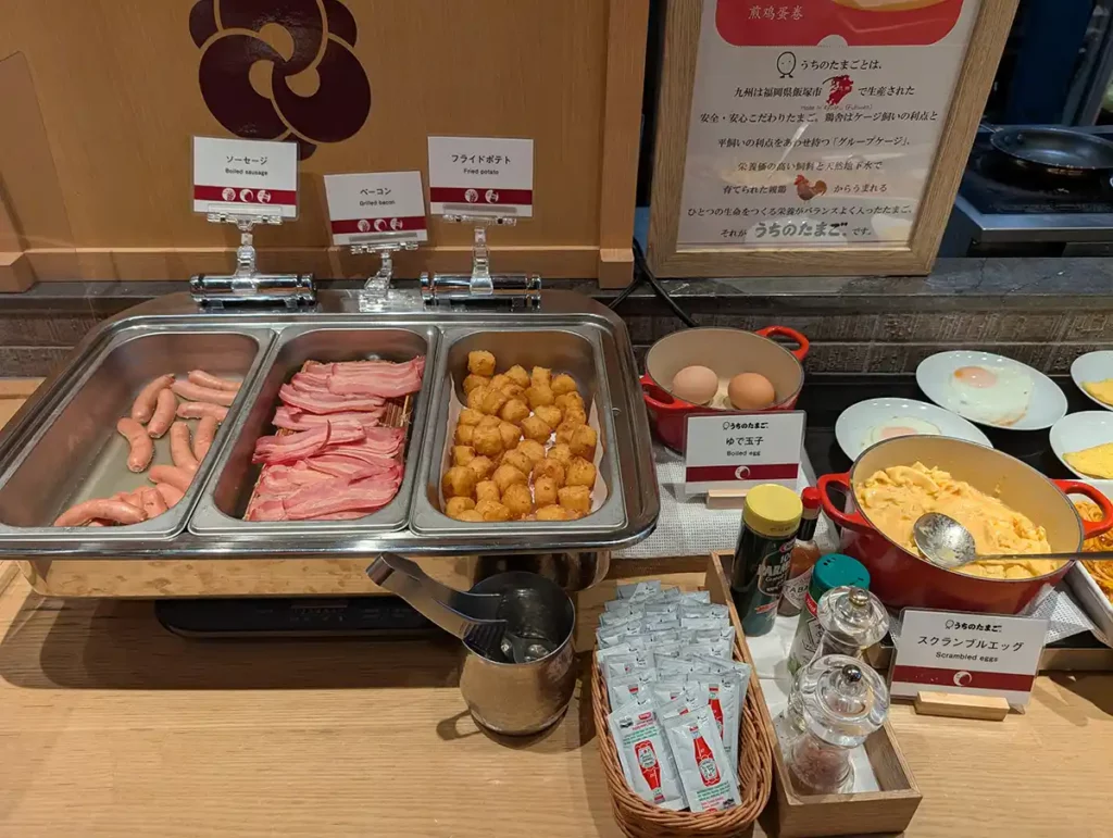 A breakfast buffet in a hotel in Shinjuku, Tokyo. There are sausages, bacon, tater tots and scrambled eggs