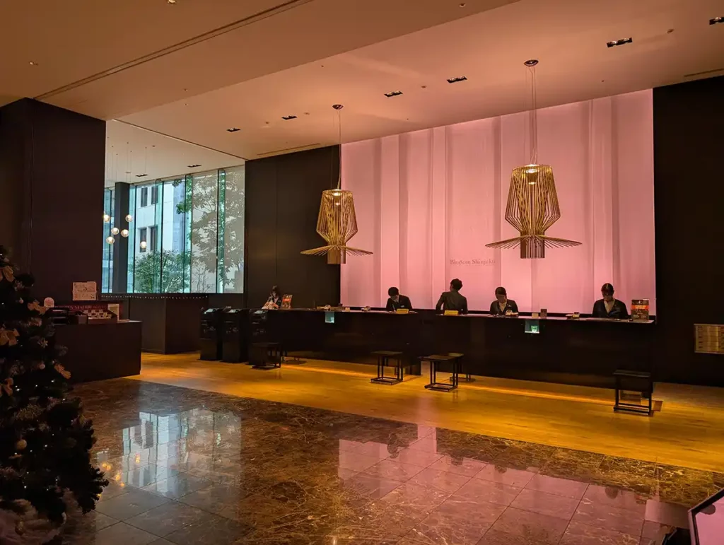 The reception desk at the JR Kyushu Blossom hotel in Shinjuku, Tokyo. A calmly lit, wide room with a long reception desk. 