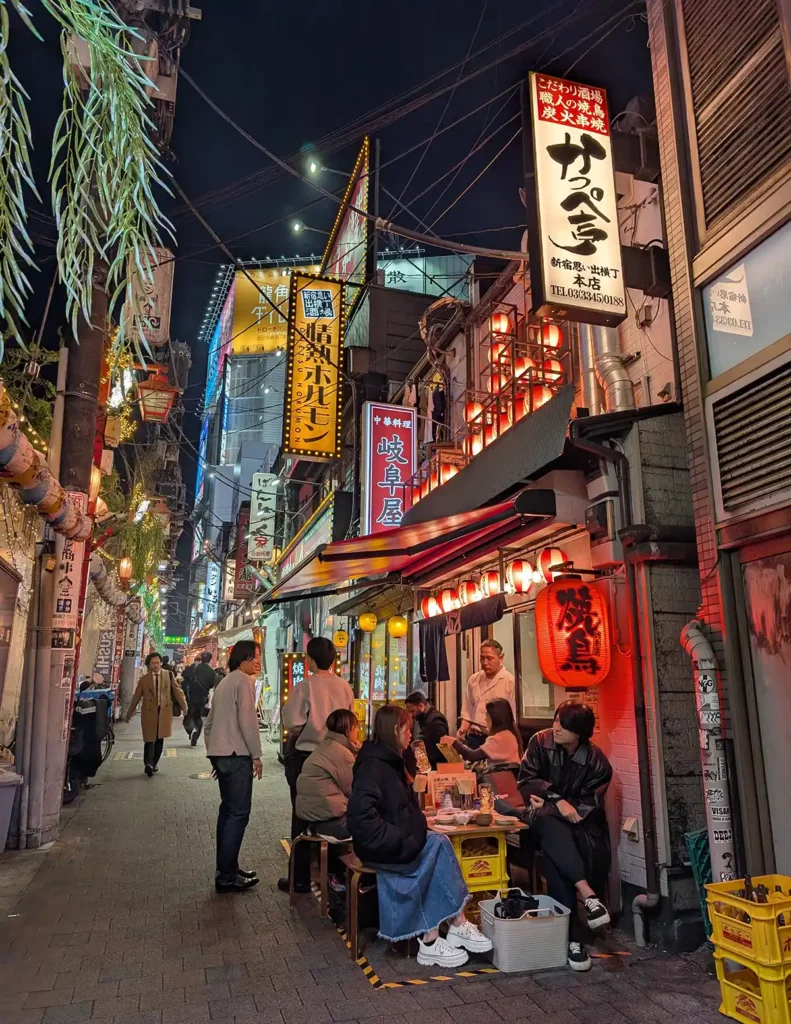 A narrow alleyway with lots of signs and people eating and drinking in a tiny bar
