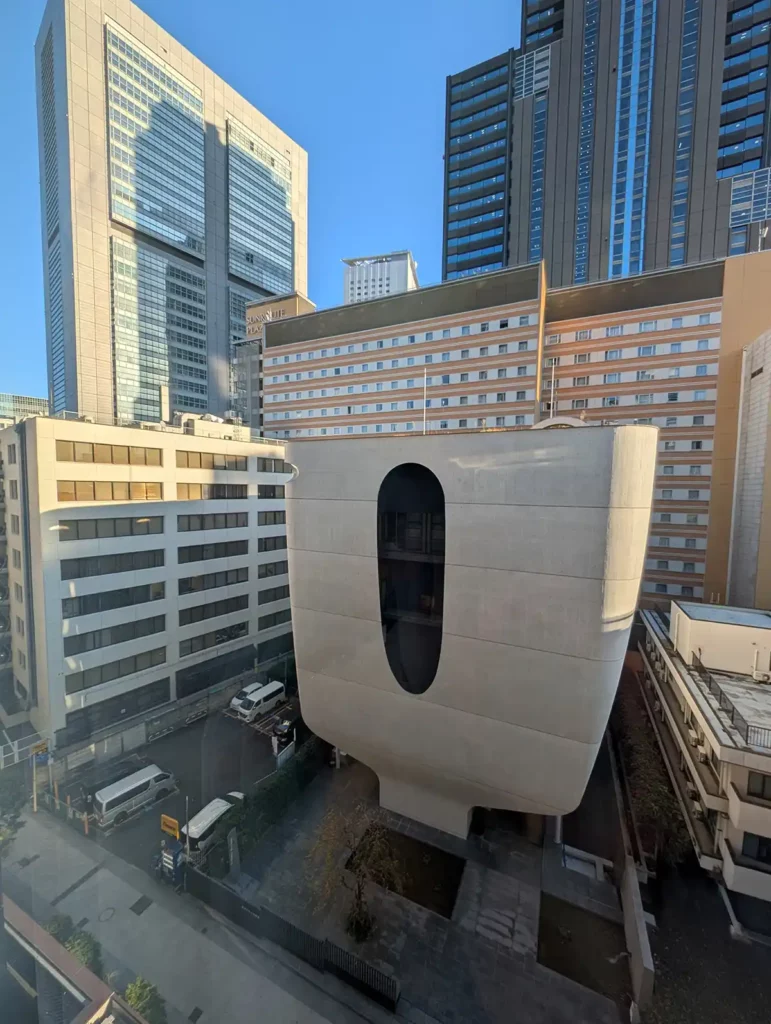 An ultra-modern, curved building made out of concrete. There are other skyscrapers and a blue sky.
