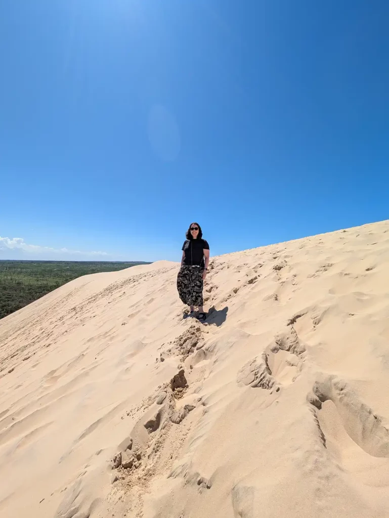 A woman (me) standing on a huge sand dune under a blue sky