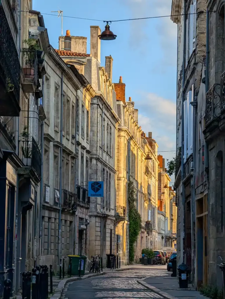 A beautiful street in Bordeaux at golden hour. Tall, golden stone buildings curve away along a narrow street.