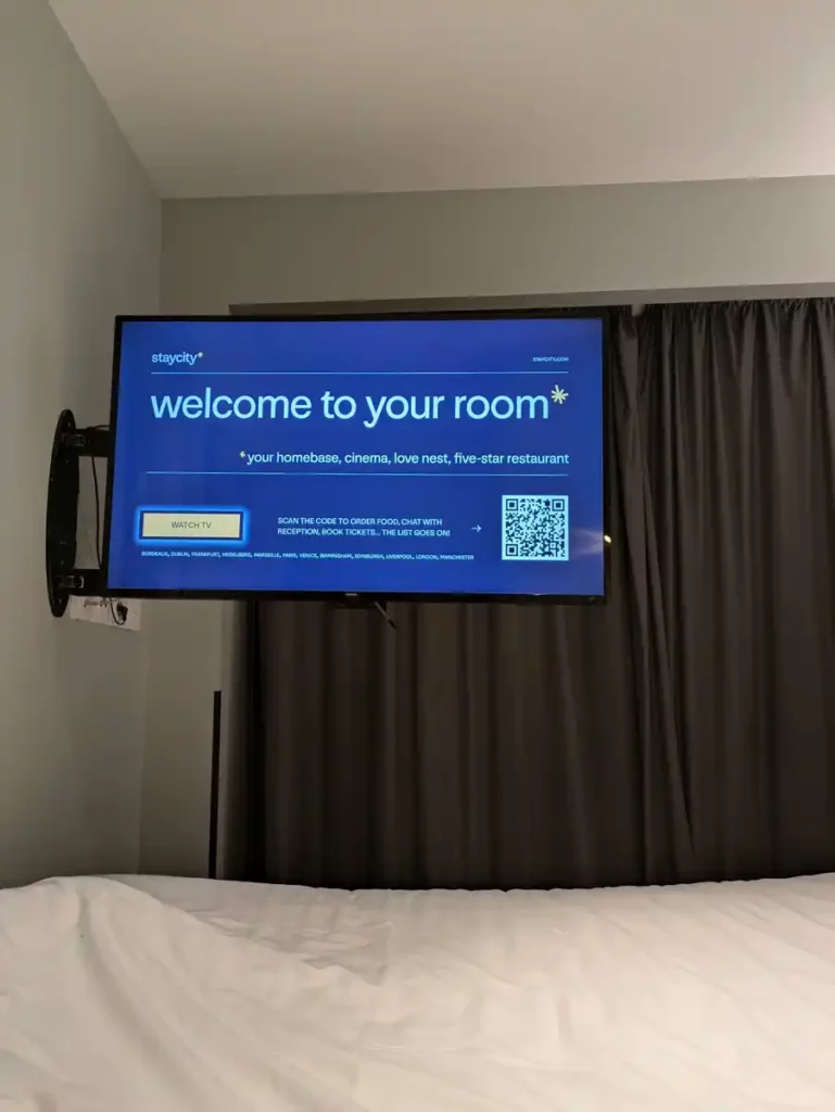 A TV which has been swung out from the wall. Someone is watching TV in bed.