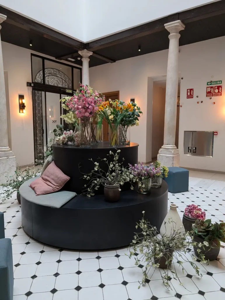 A circular seat in a large room with columns and a black and white tiled floor. There are vases of flowers everywhere.