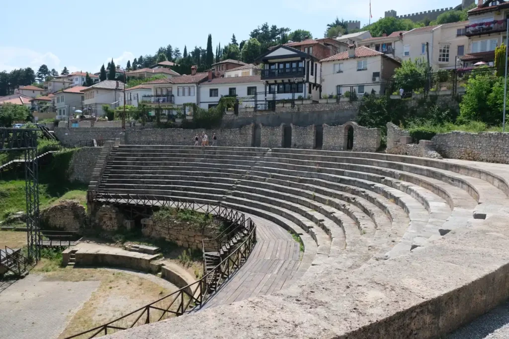 The Ancient Greek theatre in Ohrid, Macedonia. The semicircular theatre's stone seating is built into the hillside, with traditional white houses above.