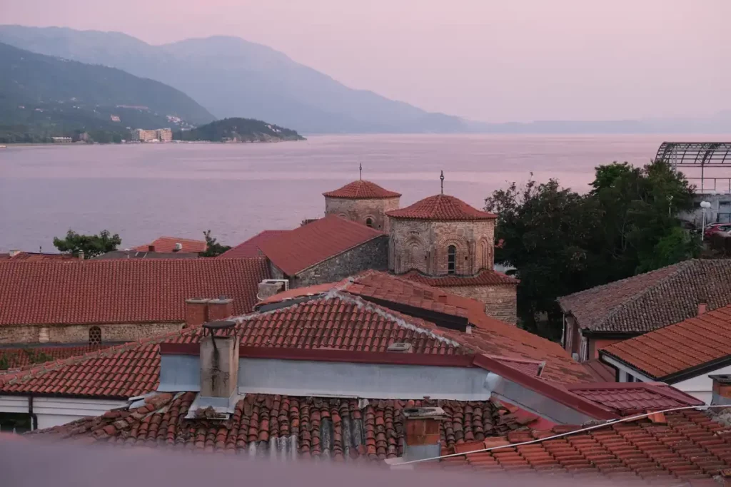 A view of Ohrid's Byzantine Saint Sophia church with the lake beyond. It's sunset and the lake is glowing purple. 