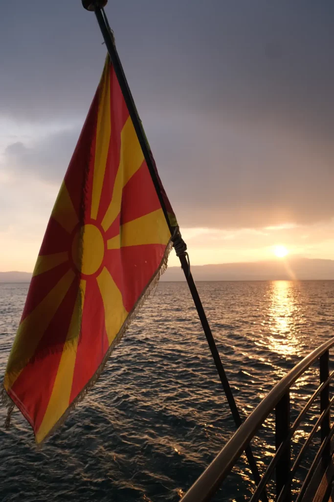 The North Macedonian flag flying from a boat on Lake Ohrid. The sunset in the background is shining across the lake and lighting up the flag. 