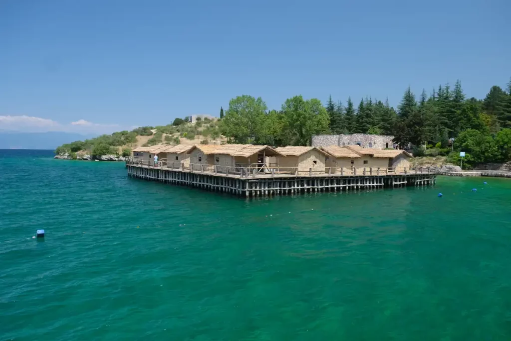 A cluster of wooden and straw houses on a wooden platform in a turquoise lake