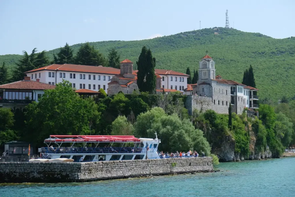 An old monastery complex on a wooded hill above a lake. There's a wharf below where another boat is docked.