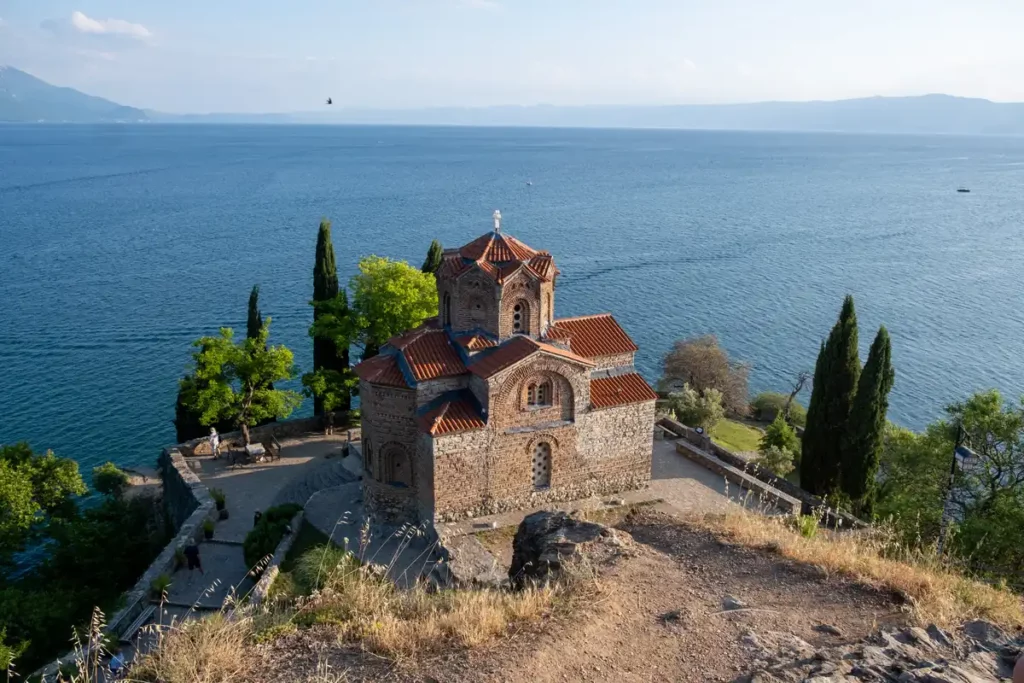 A Byzantine brick church with a red tiled roof set on a clifftop above a lake