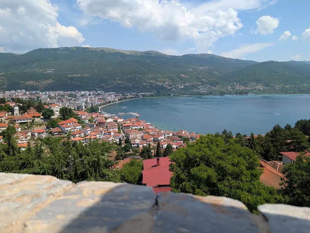 A view from Samuel's Fortress in Ohrid. There's a sweeping view over the town and lake, with mountains beyond. In the foreground, you can see the stone battlements of the castle.