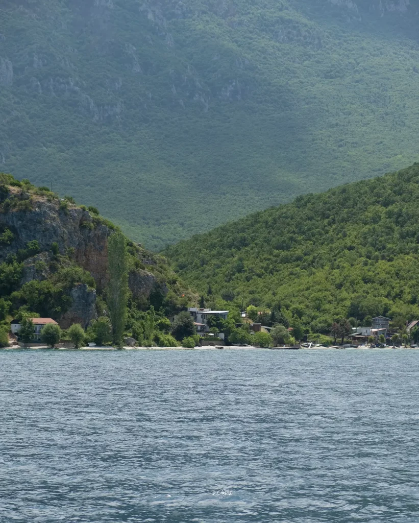 The shore of a lake, with wooded mountains rising steeply up in the background. 