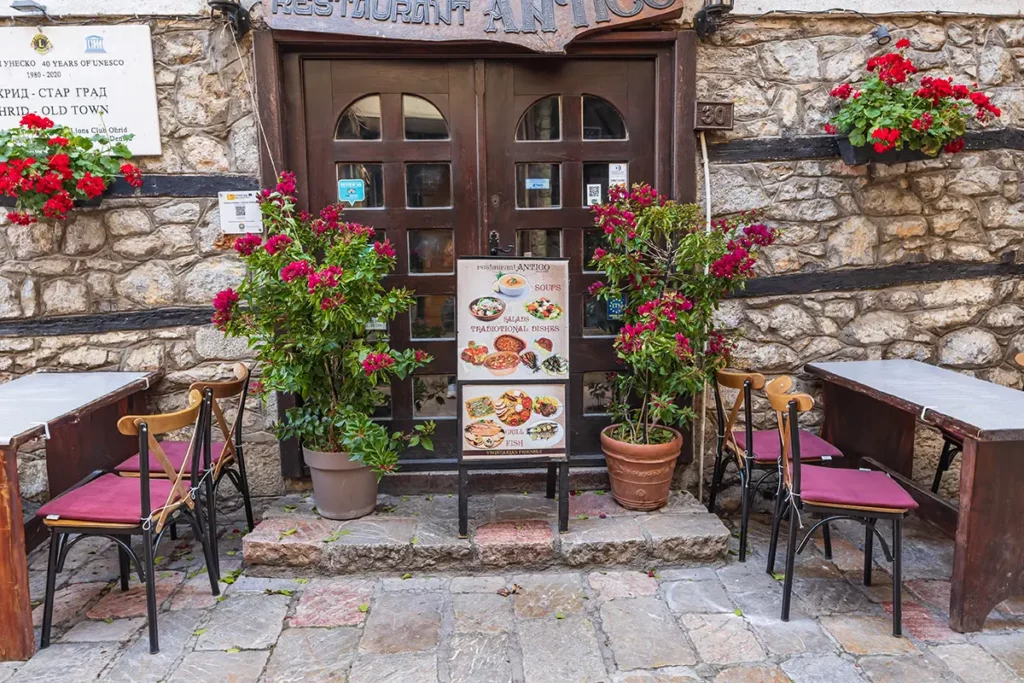 A restaurant in a rustic stone building with tables and chairs outside. There's a menu saying that they serve traditional Macedonian food.