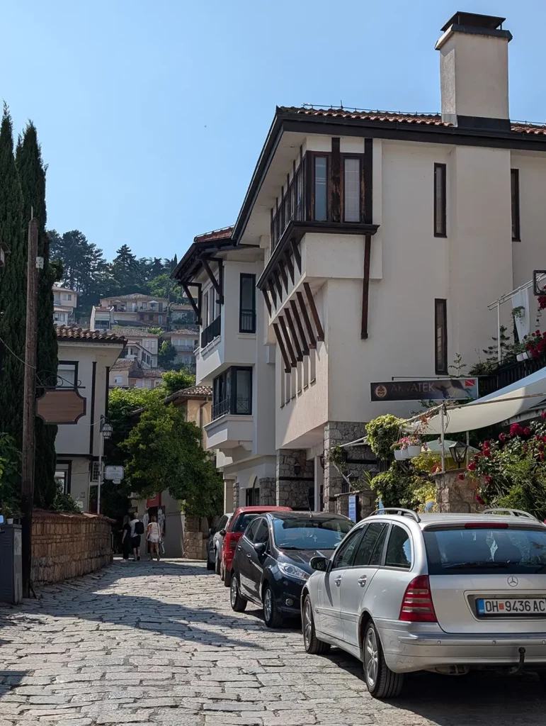 A narrow, stone-paved street with cars parked up