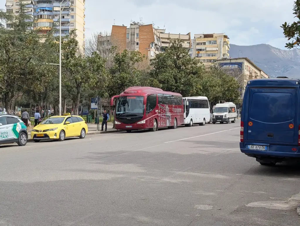 The Biblioteka bus stops at Rruga Ludovik Shllaku in the centre of Tirana. A wide street has multiple buses parked up.