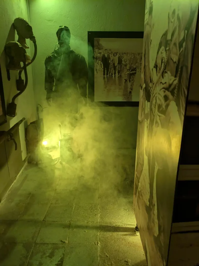 A simulation of a chemical gas attack. A soldier figure is stood in the corner of a bunker room. Green smoke is being pumped into the room. 