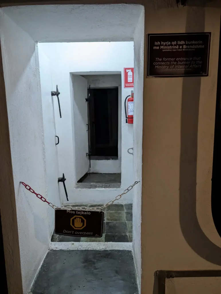 An underground bunker door. The sign beside it says that this was once the original entrance via the Albanian Ministry of the Interior building.
