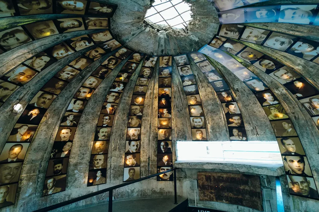 The domed roof of a concrete bunker with rows of photographs. There's a hole in the roof, as if the bunker has come under bombardment.