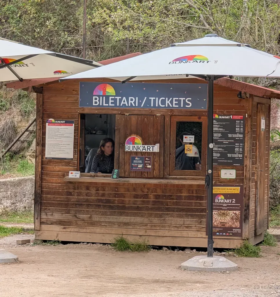 The ticket office at Bunk'Art 1. A wooden ticket office with a price list outside, a credit card sign and umbrellas to shelter customers.