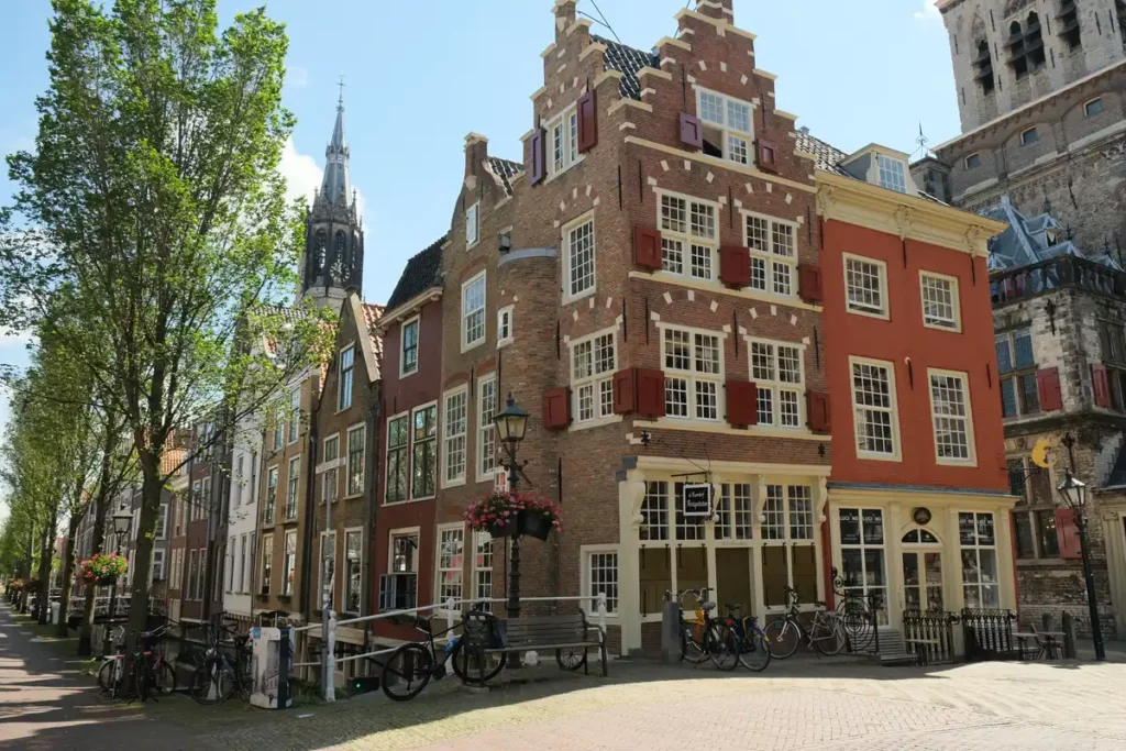 A historic street on a canal, with tall brick buildings and the spire of a church in the background