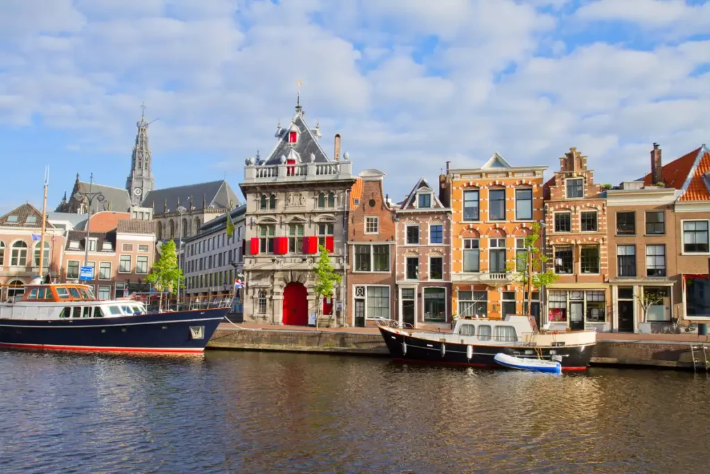 A row of colourful medieval buildings along a river, with boats in front