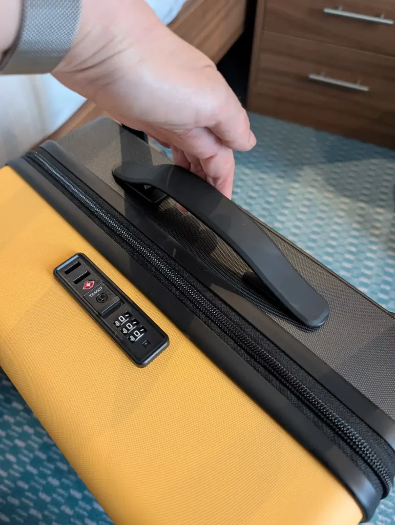 A hand pulling up a handle on top of a suitcase