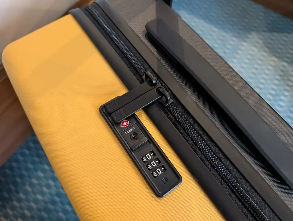 A TSA lock with code entry on top of a yellow suitcase