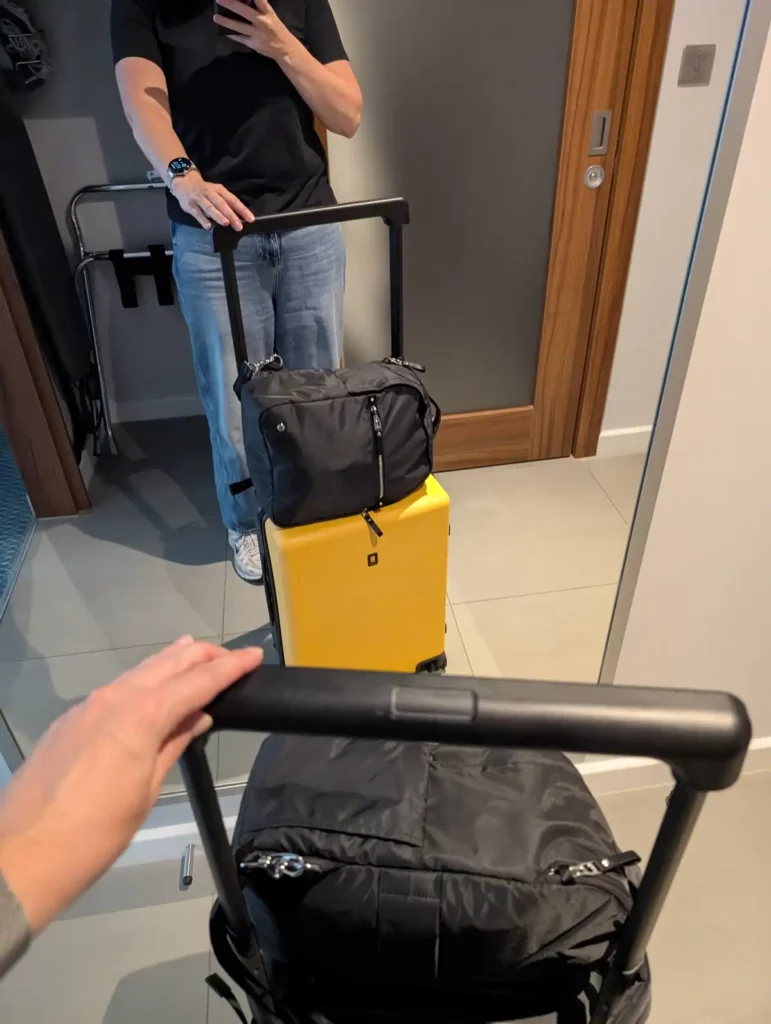 A woman holding a yellow suitcase with a backpack on the top