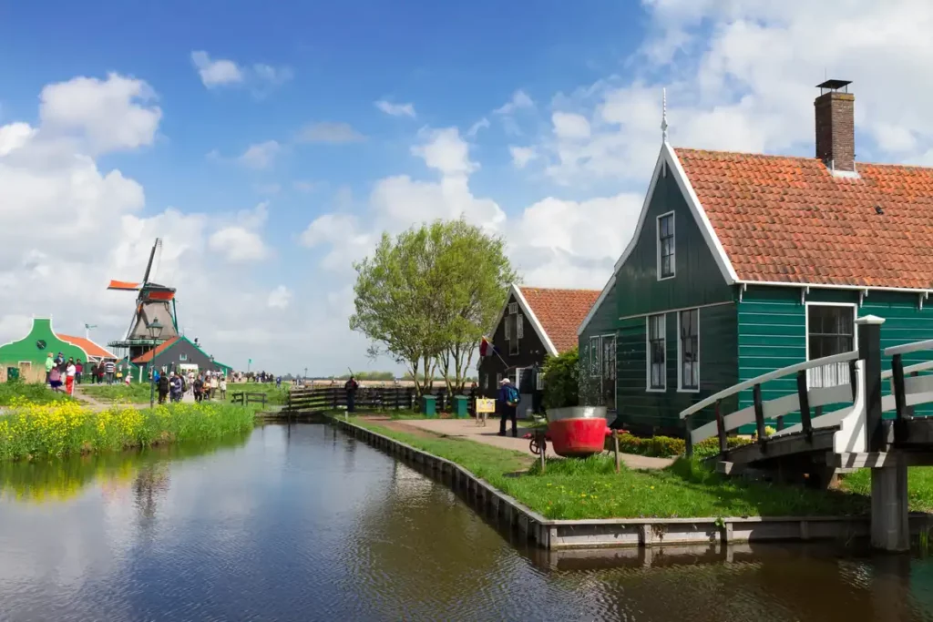 Old wooden houses, smartly painted in green with red roofs, along a canal with a windmill in the distance