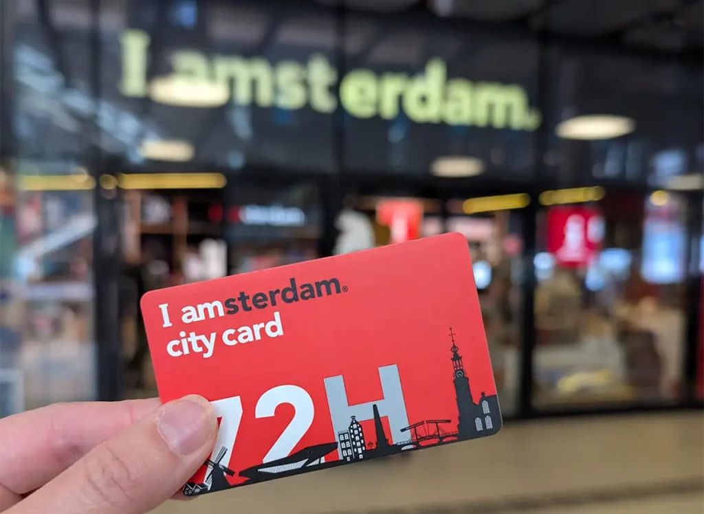 A hand holding an I amsterdam city card in front of the I amsterdam store at Centraal Station