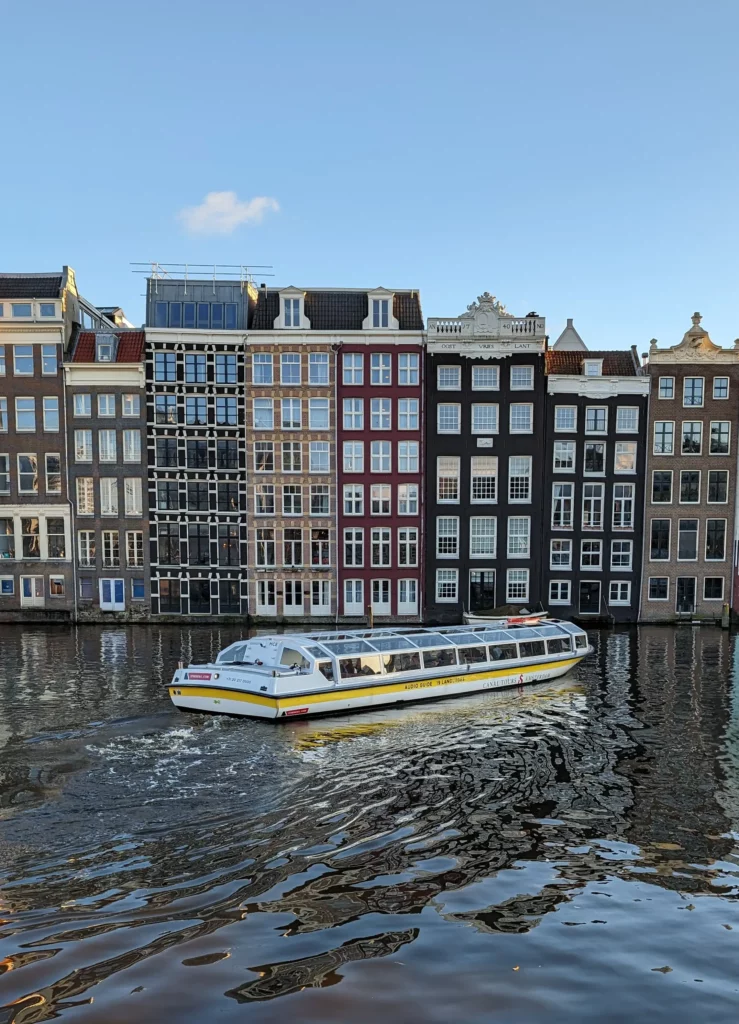 A tour boat setting off on an Amsterdam canal cruise, in front of tall canal houses.