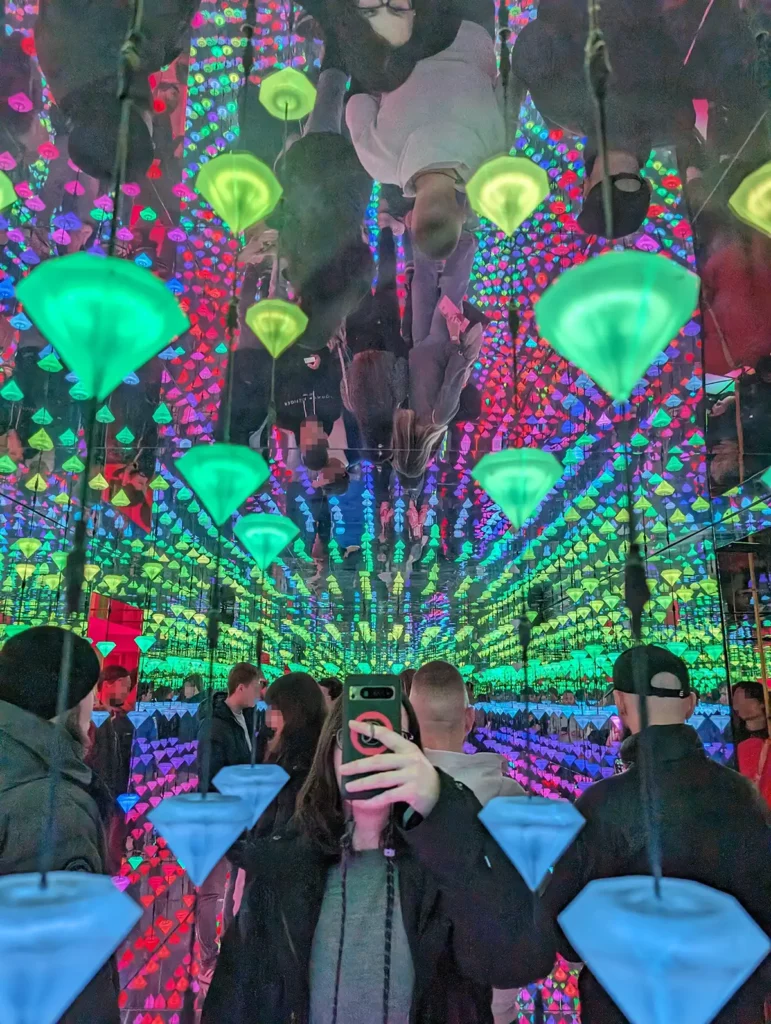 A woman holding a phone and looking into an art installation of hanging, brightly lit gems