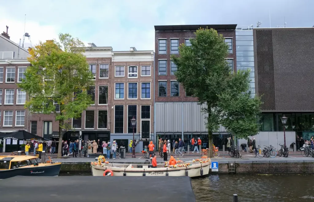 The Anne Frank House Museum by the side of the Prinsengracht canal. The building that held the Secret Annexe is to the left; to the right there is a modern museum building. A canal boat tour is dropping people off outside. 