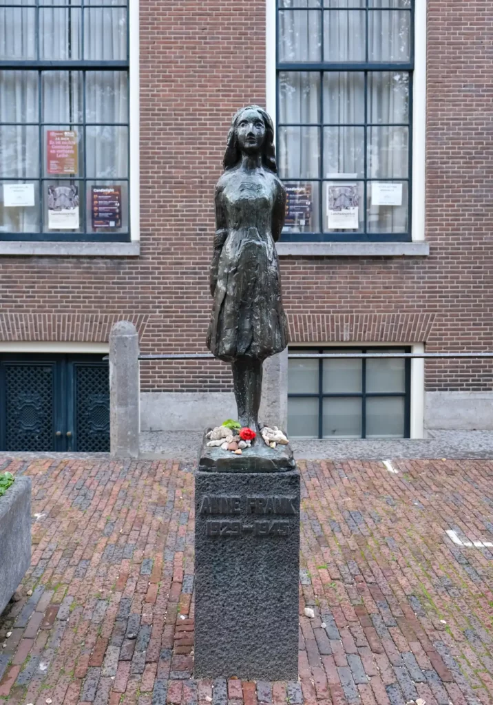A small statue of Anne Frank beside the Westerkerk in Amsterdam. Flowers have been left on the statue's plinth.