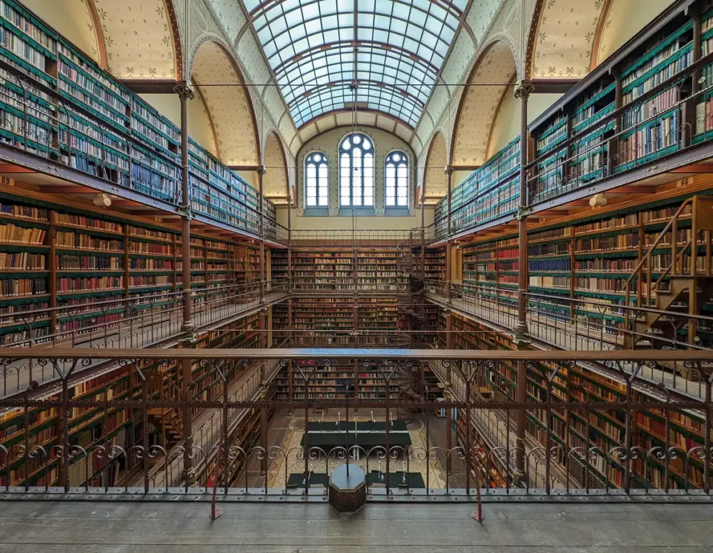A beautiful old library, with wooden shelves, galleries to walk along in front of the bookshelves and a glazed, arched roof.