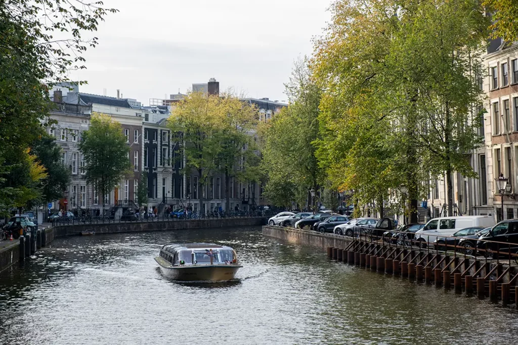 A beautiful canal scene in Amsterdam, with a tour boat passing early autumn trees and canal houses