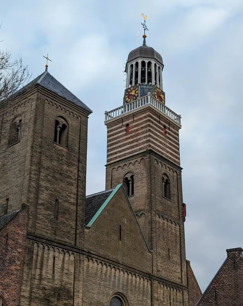 A brick-built church tower with a stripy pattern at the top and a cupola