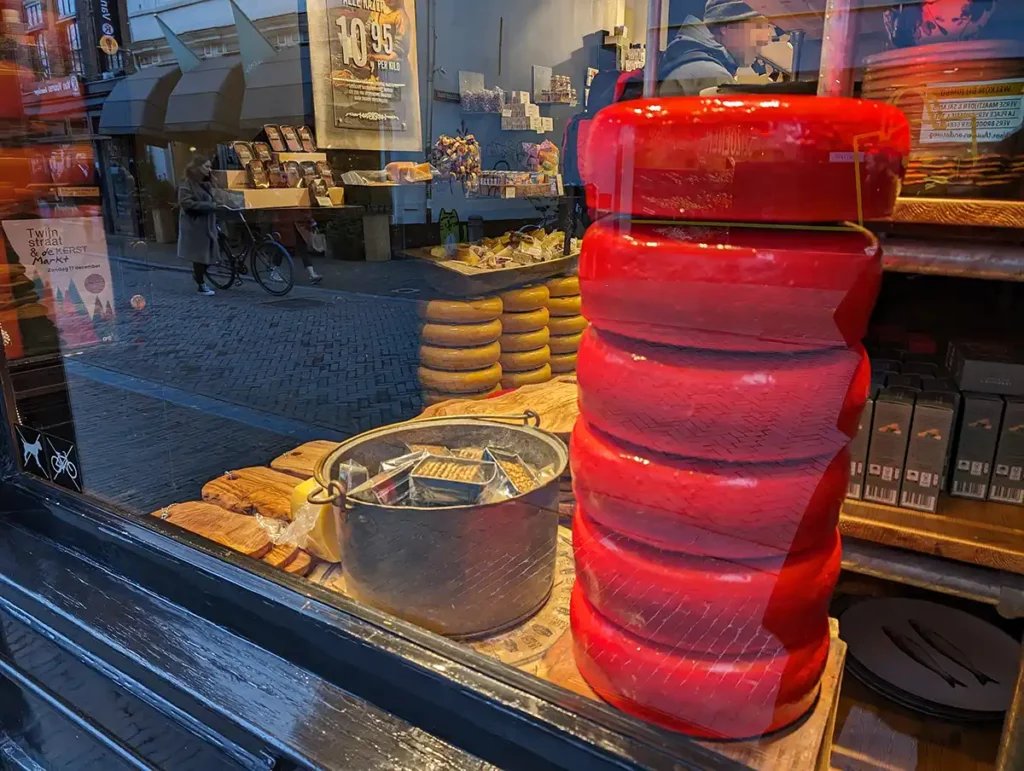 A pile of red wax-covered cheese wheels in a shop window