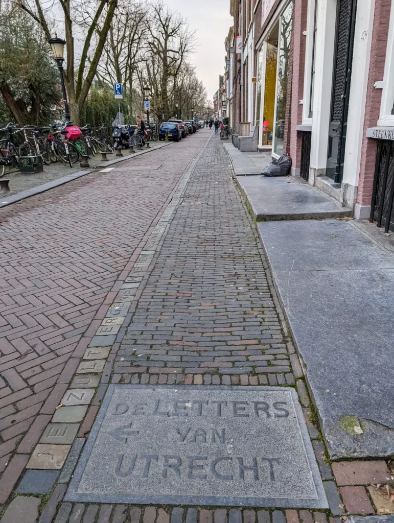 A street running beside a canal, with letters carved into stone running along the pavement