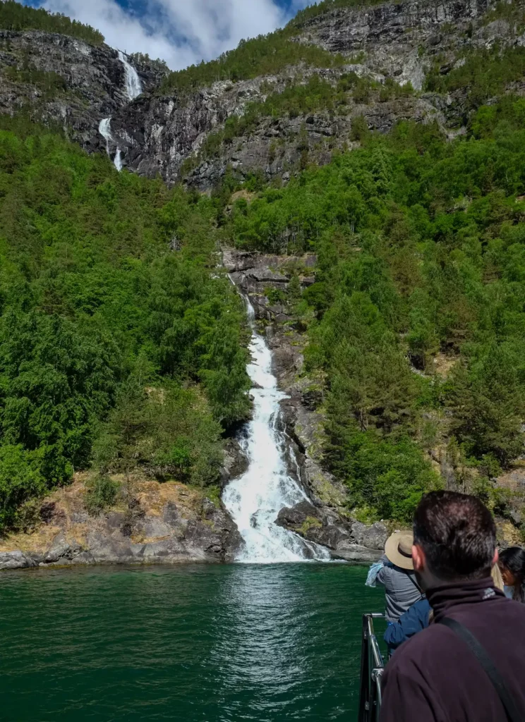 A tall waterfall crashing into the waters of the fjord