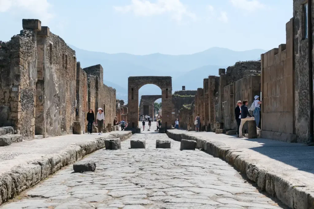 A street in Pompeii, with pavements, large stones for crossing the road and an arch in the background