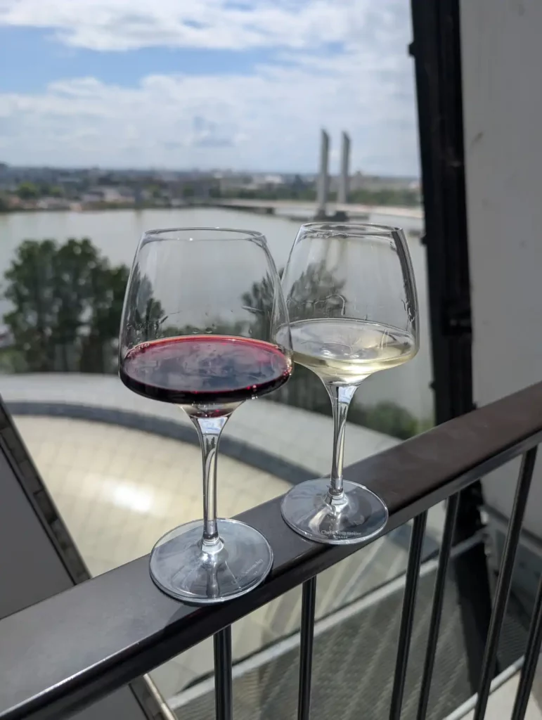 Two glasses of wine, one red, one white, on a railing overlooking a river