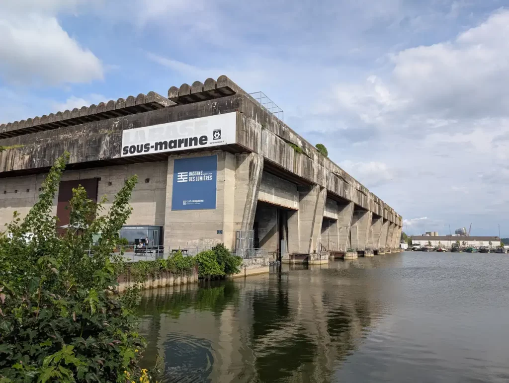 A huge concrete building by the side of a harbour, with large docks for submarines