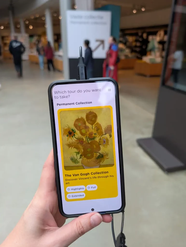 A hand holding what looks like a mobile phone, with an audio guide on the screen