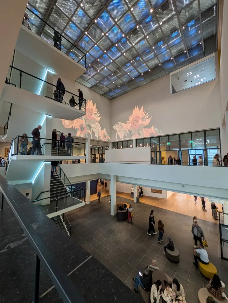 The atrium of the Van Gogh Museum, Amsterdam. There are four floors, with staircases between them. A image of Van Gogh's Sunflowers is being projected on the wall.