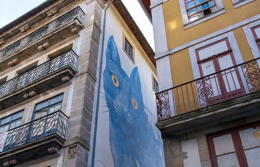 A mural of a giant blue cat, peeking out between buildings