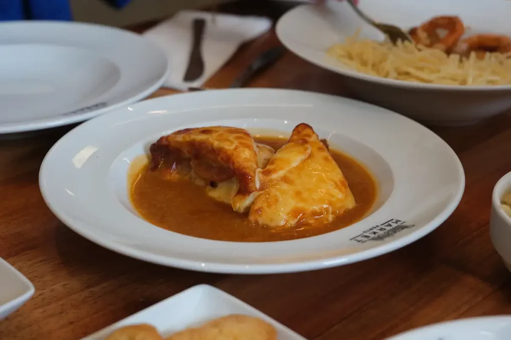 A meat sandwich with cheese on top, floating in a dish of gravy