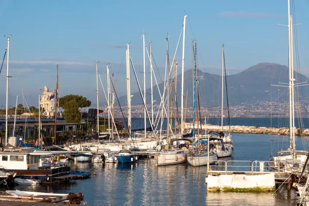 A harbour with sailing boats, with Mount Vesuvius in the background