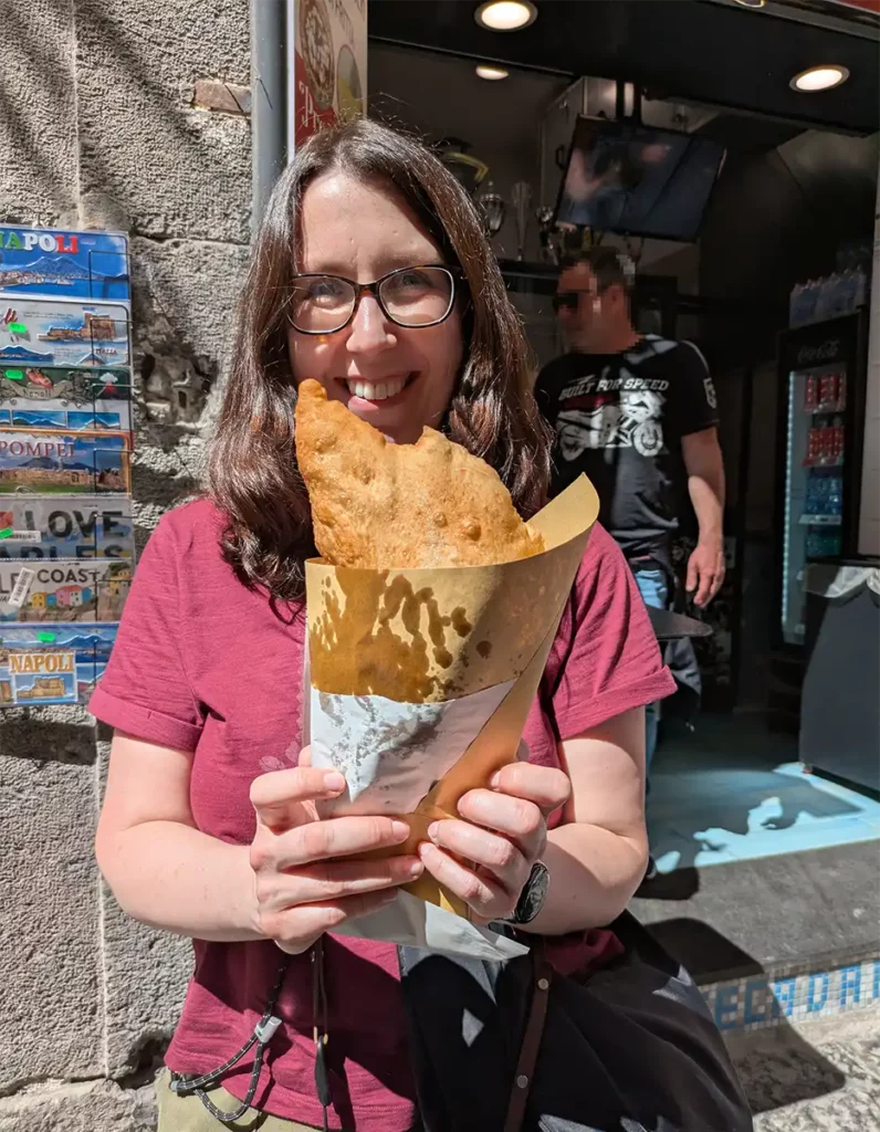 A woman with glasses holding a pizza fritta fried pizza. It's a semicircle shape and very large.